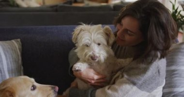 Gülümseyen beyaz kadın evdeki kanepede oturan köpeğine sarılıyor. Yaşam tarzı, evcil hayvan, arkadaşlık ve hayvansal arkadaşlık kavramı.