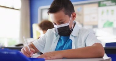 Sınıfta kameraya bakarken yüz maskesi takan melez bir öğrencinin portresi. Coronavirus covid 19 salgını sırasında ilkokuldaki çocuklar.