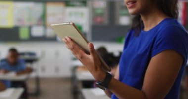 Sınıfta arka planda tablet çocukları olan mutlu bir melez kadın öğretmenin portresi. İlkokuldaki çocuklar.