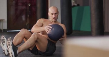 Kafkas kaslı bir adam spor salonunda ilaç topuyla karın kası egzersizi yapıyor. Spor, antrenman ve spor konsepti
