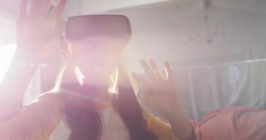 Evde oturan mutlu Asyalı kız, oturma odasında oturmuş, arka ışıklandırma ve video kamera kullanarak eğleniyor. Karantina süresince evde tecrit altında..