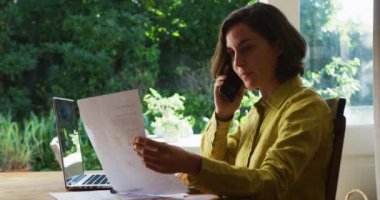 Beyaz bir kadının evde çalışırken bilgisayarla akıllı telefondan konuştuğu bölüm. Evde karantina sırasında ve ev konseptinden çalışırken..