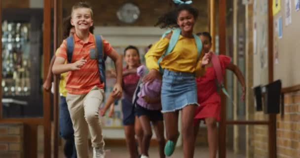 Różnorodna Grupa Szczęśliwych Uczniów Noszących Plecaki Biegnących Szybko Szkolnym Korytarzem — Wideo stockowe