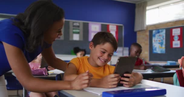 Diverse Smiling Female Teacher Helping Schoolboy Sitting Classroom Using Tablet — Stock Video