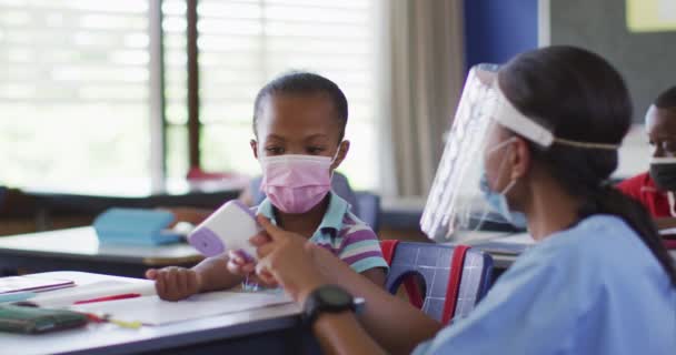 温度を測定する方法を学童を示す多様な医療従事者は すべての顔のマスクを着て コロナウイルス感染症の小学生の子供たちは — ストック動画