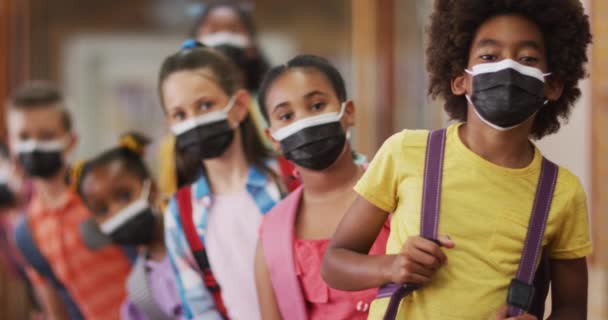 キューに立っている多様な子供たちは すべての顔のマスクを着用 コロナウイルス感染症の小学生の子供たちは — ストック動画