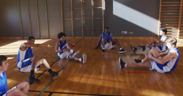 青いスポーツウェアとストレッチを身に着けている多様な男性バスケットボールチーム バスケットボール室内裁判所でのスポーツトレーニング — ストック動画