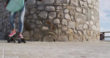 Deniz kenarında güneşli bir gezinti güvertesinde sörf tahtası taşıyan mutlu ırklı kadın kaykaycılar. Sağlıklı yaşam, gözden uzak ve doğaya yakın..