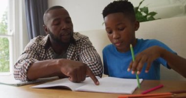 Mutlu Afro-Amerikan babası mutfak masasında oturup oğluna ödevlerinde yardım ediyor. Aile evde birlikte vakit geçiriyor..