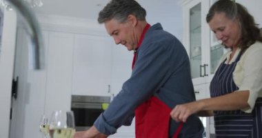 Mutfaktaki son sınıf beyaz çift, karı koca önlüklerini bağlıyor ve gülümsüyor. evde birlikte emeklilik hayatı.