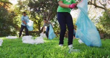 Gülümseyen beyaz kız elinde çöp torbası, ebeveynleriyle plastik atık topluyor. Çevre koruma gönüllüleri kırsal alanda temizlik yapıyor..