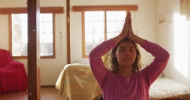 Rahatlamış melez kadın yoga yapıyor, güneşli kır evinde meditasyon yapıyor ve gülümsüyor. Şehir dışında, kırsal kesimde basit sağlıklı yaşam..