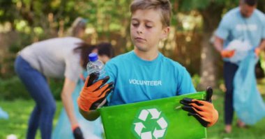 Gülümseyen Kafkas oğlu dışarıda elinde geri dönüşüm kutusuyla aileleriyle plastik atık topluyor. Çevre koruma gönüllüleri kırsal alanda temizlik yapıyor..