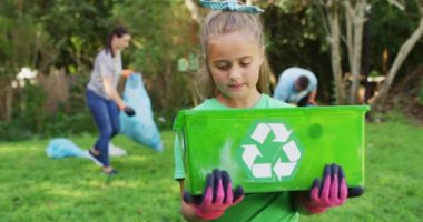 Gülümseyen beyaz kız dışarıda elinde geri dönüşüm kutusuyla anne babasıyla plastik atık topluyor. Çevre koruma gönüllüleri kırsal alanda temizlik yapıyor..