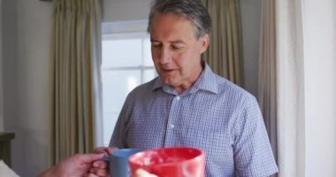 Oturma odasında pencereden dışarı bakıp kahve içip sohbet eden son sınıf beyaz çifti. emeklilik yaşam tarzı evde.