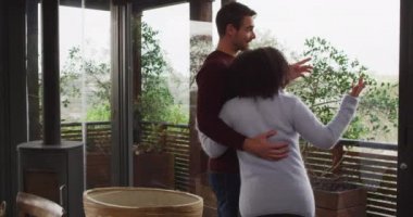 Gülümseyen karışık ırk çifti tatil evindeki balkonda yan yana dururken manzaranın tadını çıkarıyor. çift balayı ve tatil konsepti