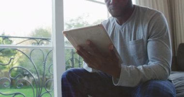 Afrikalı Amerikalı adam evdeki kanepede otururken dijital tablet kullanıyor. Evde tek başına kalmak.