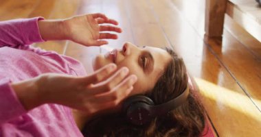 Kulaklık takan, oturma odasında uzanmış gülümseyen mutlu melez kadın. Karantina süresince evde tecrit altında..