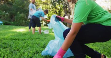 Gülümseyen beyaz kız elinde çöp torbası, ebeveynleri ve kardeşleriyle plastik atık topluyor. Çevre koruma gönüllüleri kırsal alanda temizlik yapıyor..