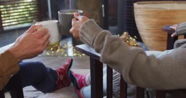 Karışık ırk çifti, yazlık evde şöminenin yanında otururken kahve içip kadeh kaldırıyor. çift balayı ve tatil konsepti