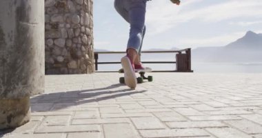 Deniz kenarındaki güneşli gezinti güvertesinde kaykay yapan melez bir kadının arka görüntüsü. Sağlıklı yaşam, gözden uzak ve doğaya yakın..