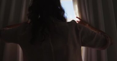 Üst düzey beyaz kadın güneşli odada perde çekiyor ve pencereden dışarı bakıyor. evde emeklilik yaşam tarzında.