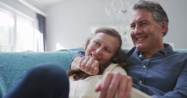 Oturma odasında oturup televizyon izleyen ve konuşan Kafkasyalı mutlu bir çift. evde birlikte emeklilik hayatı.