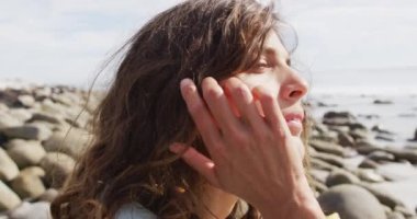 Düşünceli melez kadın sahilde oturmuş, manzaranın tadını çıkarıyor ve gülümsüyor. Sağlıklı yaşam, gözden uzak ve doğaya yakın..