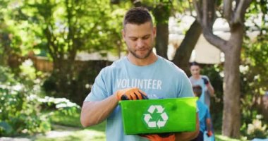 Elinde geri dönüşüm sandığı tutan, plastik atık toplayan gönüllü tişört giyen gülümseyen beyaz adam. Çevre koruma gönüllüleri kırsal alanda temizlik yapıyor..