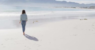 Sahilde çıplak ayakla yürüyen melez bir kadının arka görüntüsü. Sağlıklı yaşam, gözden uzak ve doğaya yakın..