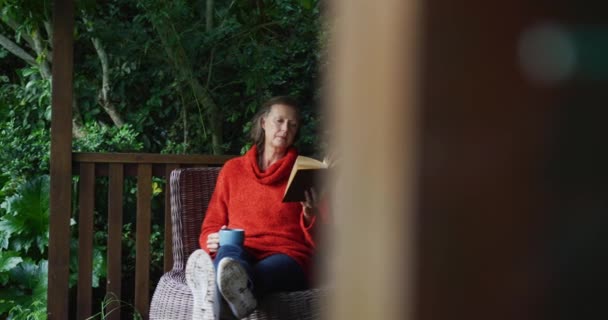 シニア白人女性は庭でリラックスし 足で座ってコーヒーを飲み 本を読む 家庭での退職生活だけで — ストック動画