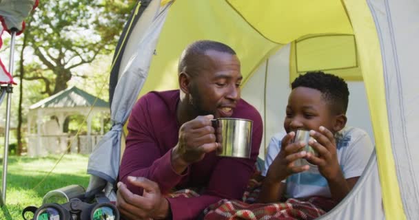 庭で一緒にテントの中でアフリカ系アメリカ人の父と息子がコーヒーを試飲し 飲んでいます 父親と愛の概念 — ストック動画