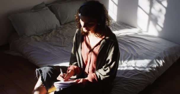沉思的混血女子坐在床上 在阳光灿烂的茅屋卧室里写作 简单地生活在远离电网的农村家庭中 — 图库视频影像