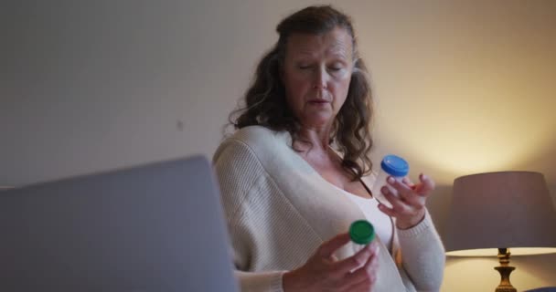 迷惑不解的资深高加索女人拿着两瓶药片打咨询视频电话 远程医疗 家庭在线保健 — 图库视频影像