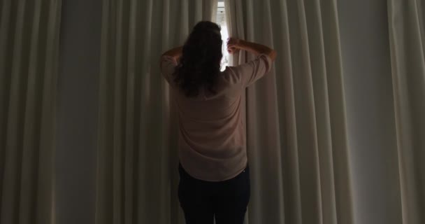 日当たりの良い部屋でカーテンを描画し 窓の外を見てシニア白人女性の背面図 家庭での退職生活 — ストック動画