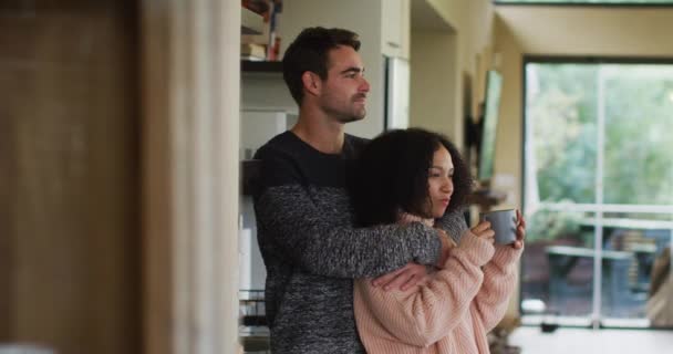 快乐而多样化的夫妻在厨房里拥抱和喝咖啡 在家里一起消磨时光 — 图库视频影像