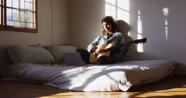 在阳光充足的茅屋卧室里 坐在床上弹奏吉他的混血儿松了口气 简单地生活在远离电网的农村家庭中 — 图库视频影像