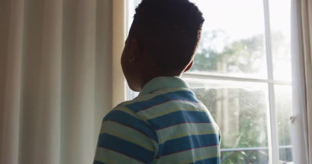 Niño Afroamericano Abriendo Cortina Mirando Por Ventana Soleada Retroiluminado Por — Vídeo de stock