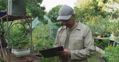 Bahçe merkezinde notlar alan melez erkek bahçıvan. Bonsai çocuk yuvasında çalışmak, küçük bir uzmanlık alanı..