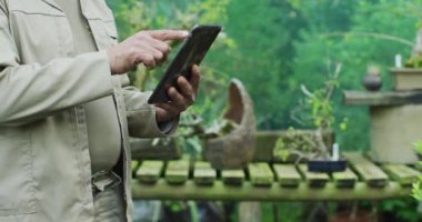 Bahçe merkezinde tablet kullanan beyaz erkek bahçıvanın orta kesimi. Bonsai çocuk yuvasında çalışmak, küçük bir uzmanlık alanı..