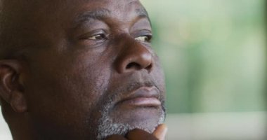 Düşünceli Afrikalı Amerikalı kıdemli bir adam çenesini tutup pencereden dışarı bakıyor ve gülümsüyor. Emeklilik hayatı, evde yalnız zaman geçirmek..