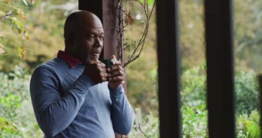 Afrika kökenli Amerikalı son sınıf öğrencisi balkonda durmuş kahve içiyor, gülümsüyor ve el sallıyor. Emeklilik hayatı, evde yalnız zaman geçirmek..