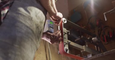 Kafkasyalı erkek bıçak imalatçısının atölyede elinde bıçak ve zımpara makinesi varken yakın plan. Bağımsız küçük işletmeci iş başında.