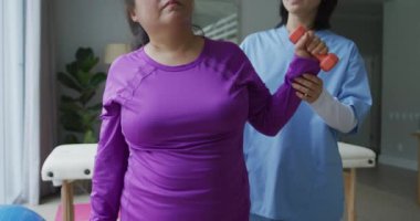 Asyalı kadın fizyoterapist kadın hastaya ameliyatta kollarını dambıllarla çalıştırmasında yardım ediyor. fizyoterapi, sağlık ve sağlık hizmetleri.