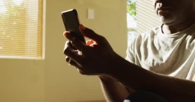 Düşünceli Afrikalı Amerikalı son sınıf öğrencisi evinde oturmuş akıllı telefon kullanıyor. Emeklilik hayatı, evde yalnız zaman geçirmek..