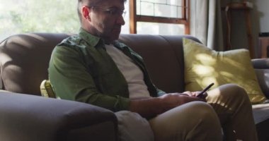 Kanepede oturan beyaz bir adam, evde akıllı telefon kullanıyor. ev hayatı ve boş zaman kavramı.