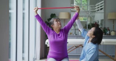 Asyalı kadın fizyoterapist ameliyatta kadın hastaya egzersiz bandıyla yardım ediyor. fizyoterapi, sağlık ve sağlık hizmetleri.