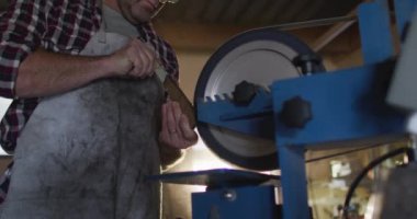 Kafkas erkek bıçak imalatçısı atölyede gözlüklü ve zımpara makinesi kullanıyor. Bağımsız küçük işletmeci iş başında.