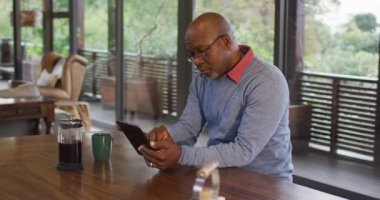 Afro-Amerikan son sınıf öğrencisi mutfakta oturmuş tablet kullanıyor. Emeklilik hayatı, evde yalnız zaman geçirmek..