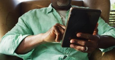 Oturma odasında tablet kullanarak oturan Afrikalı Amerikalı son sınıf öğrencisi. Emeklilik hayatı, evde yalnız zaman geçirmek..